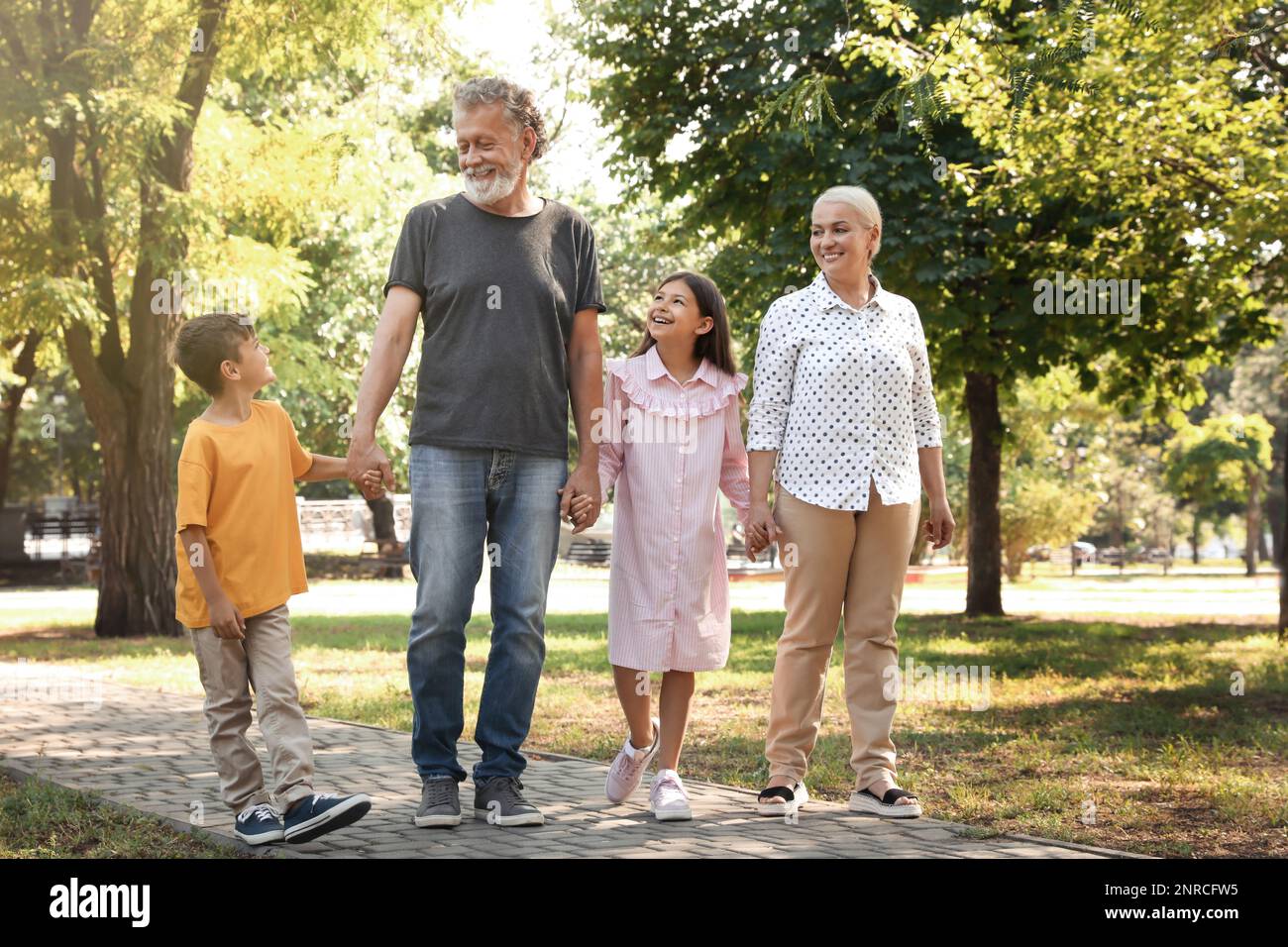 Abuelos felices con niños pequeños caminando juntos en el parque Foto de stock