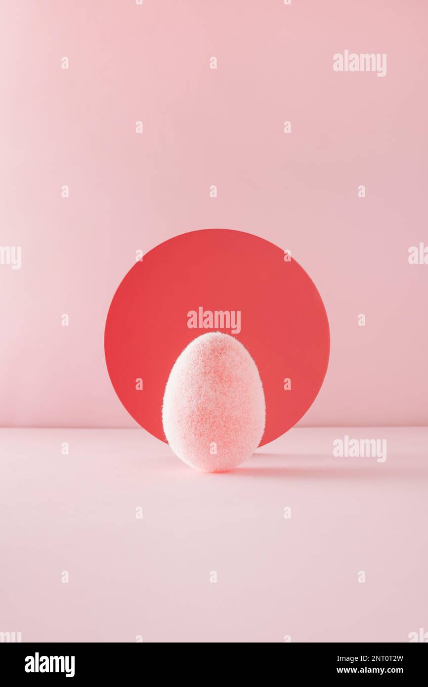 Huevo rosa esponjoso suave delante del telón de fondo rojo del círculo sobre fondo rosa. Concepto de Pascua mínimo. Foto de stock