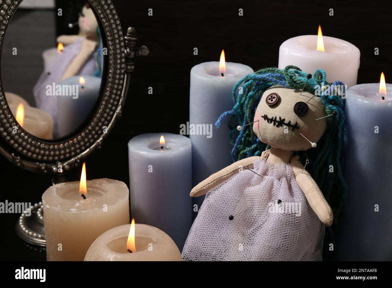 Muñeca vudú perforada con alfileres y velas sobre fondo negro. Ceremonia de la maldición Foto de stock