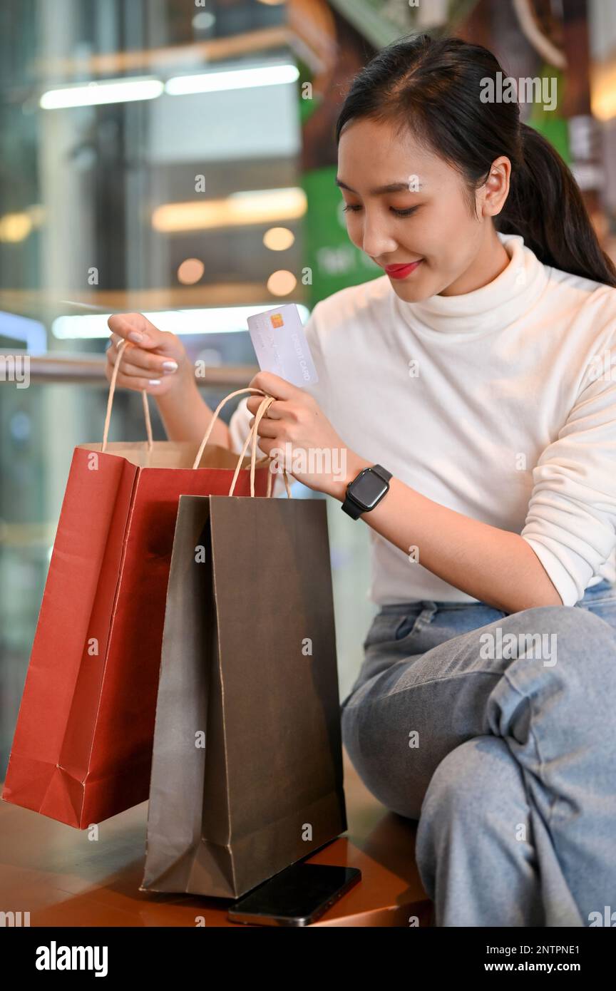 Hermosa mujer asiática en ropa casual sosteniendo una tarjeta de crédito,  abriendo sus bolsas de compras y comprobando su ropa comprada mientras  descansa en el centro comercial Fotografía de stock - Alamy