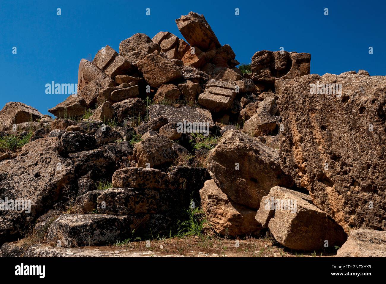 Montones de piedra caída, algunos bloques cortados con ranuras de fijación, ranuras y canales, se encuentran en el sitio del Templo de Zeus Olímpico en el Valle de los Templos, parte de la antigua ciudad griega de Akragas en Agrigento, Sicilia, Italia. El templo dórico, uno de los más grandes del mundo, data del 480 a. C., pero quedó inacabado cuando Cartago saqueó Akragas y su destrucción se completó por terremotos posteriores. Foto de stock