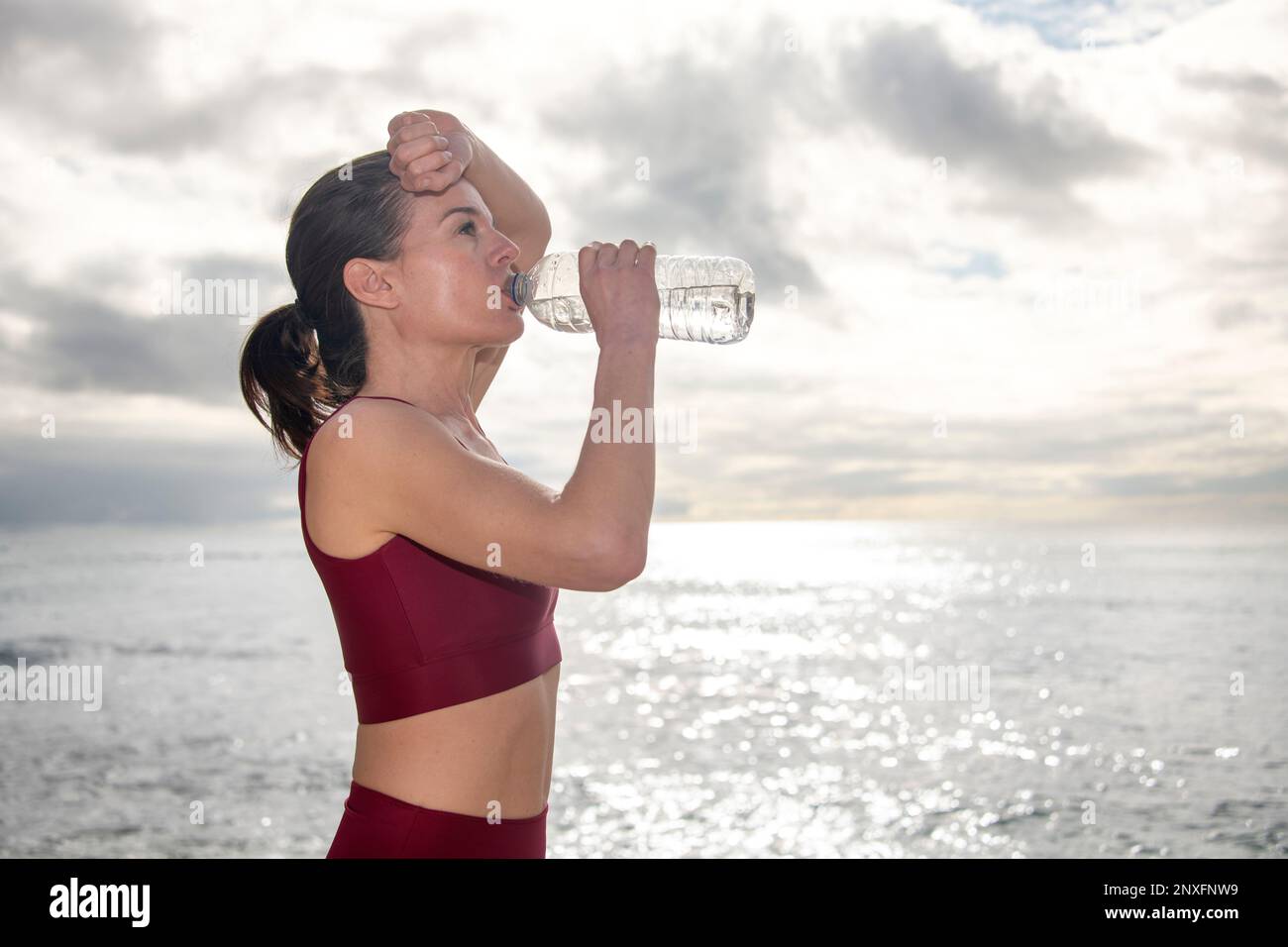 Mujer deportiva tomando un trago de agua de una botella después de teñir o correr fuera por el océano Foto de stock