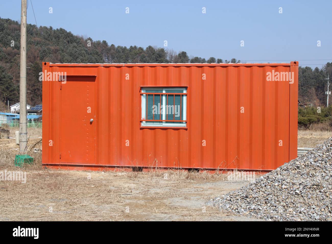 Contenedor de envío naranja brillante en el sitio de construcción Foto de stock