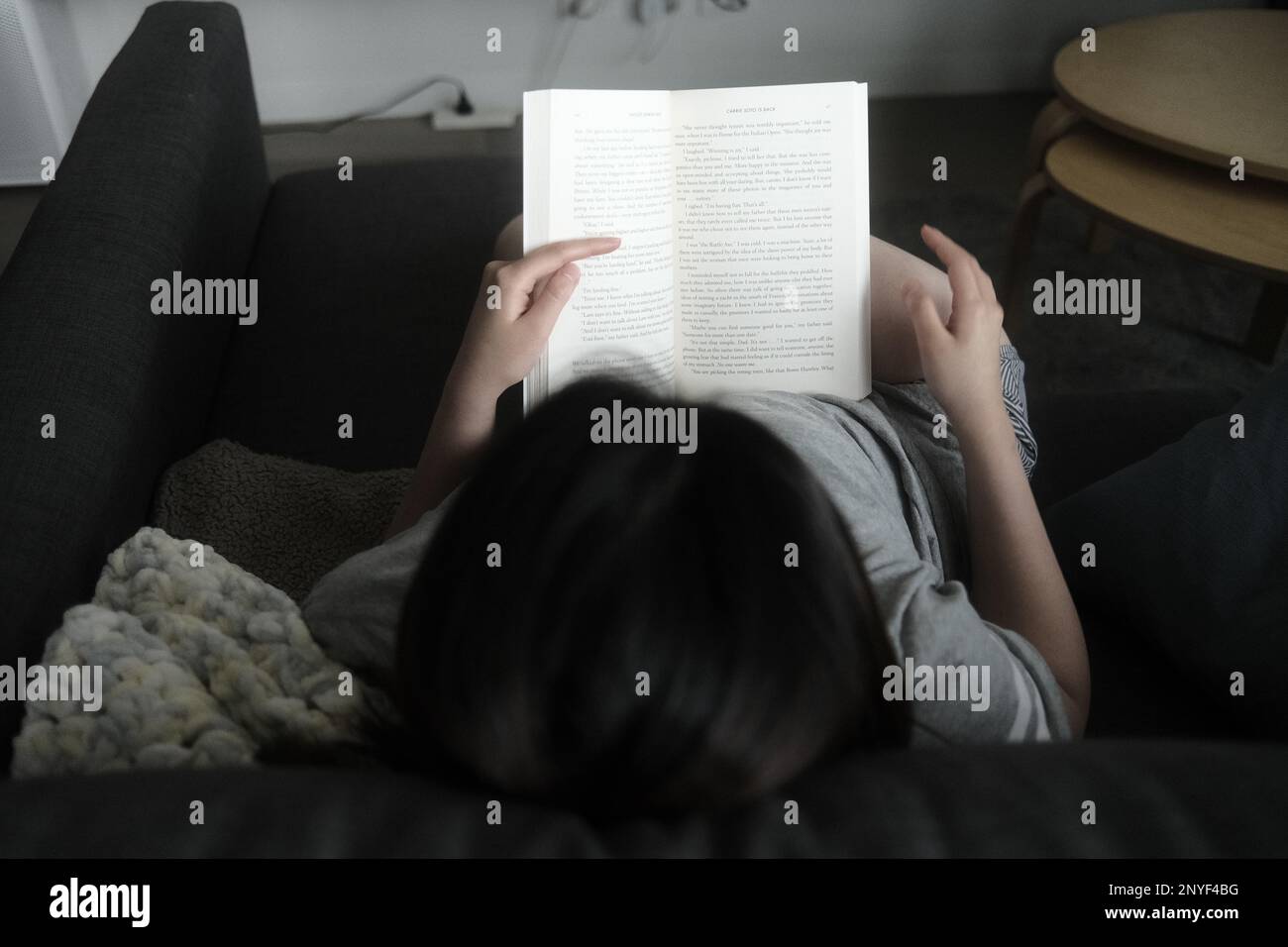 Foto de niña leyendo en un sofá en casa en un día perezoso Foto de stock