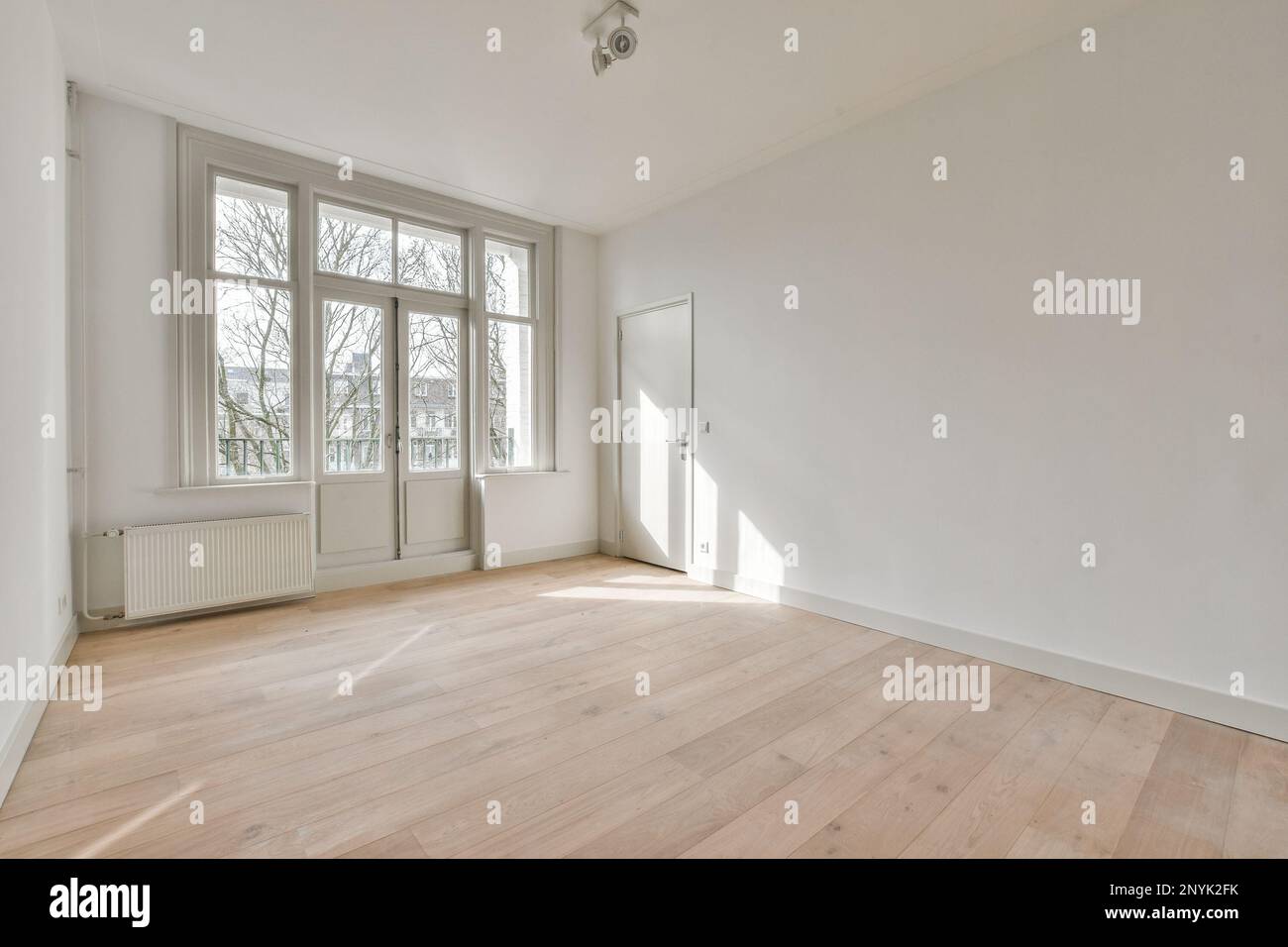 una habitación vacía con pisos de madera y grandes ventanas en las esquinas a la izquierda es una pared blanca Foto de stock