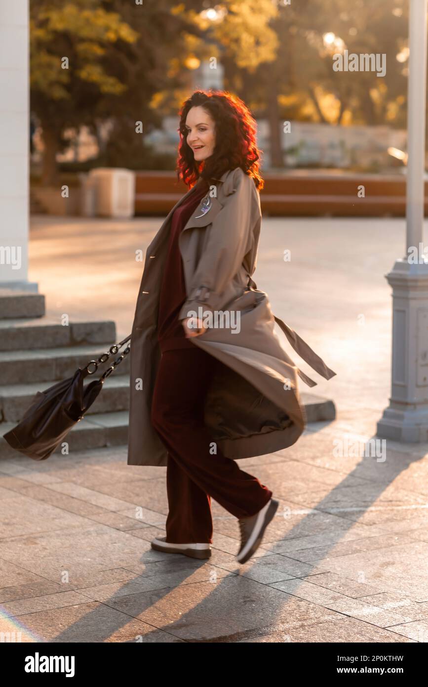 Retrato de moda al aire libre de la mujer morena de moda elegante joven,  modelo en sombrero con estilo, gargantilla y impermeable ligero posando en  la puesta del sol en Europa Fotografía