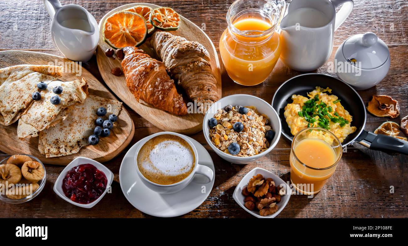 El desayuno se sirve con café, zumo de naranja, huevos revueltos, cereales, tortitas y cruasanes. Foto de stock