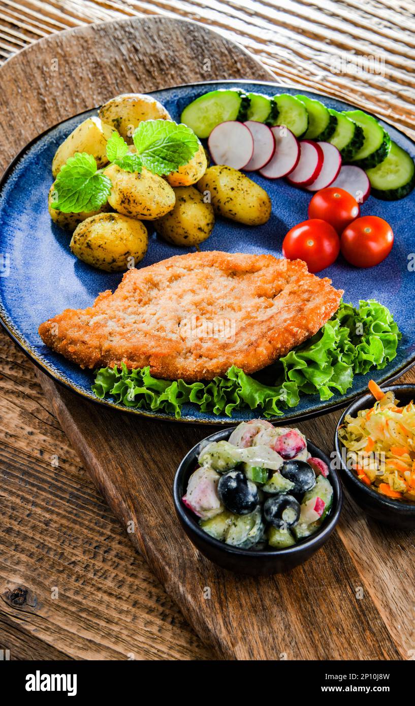 Chuleta empanada de cerdo recubierta de migas de pan con patatas y ensaladas de verduras Foto de stock