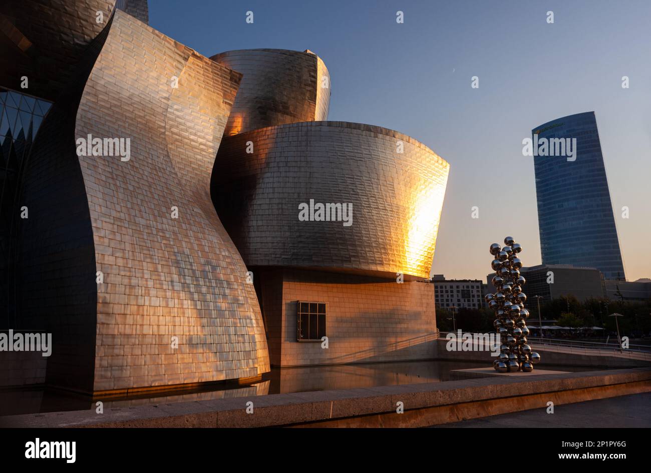Bilbao, España - 02 de agosto de 2022: Vista al atardecer del Museo Guggenheim diseñado por Frank Gehry junto a la obra de arte titulada Árbol alto y el ojo di A. Foto de stock