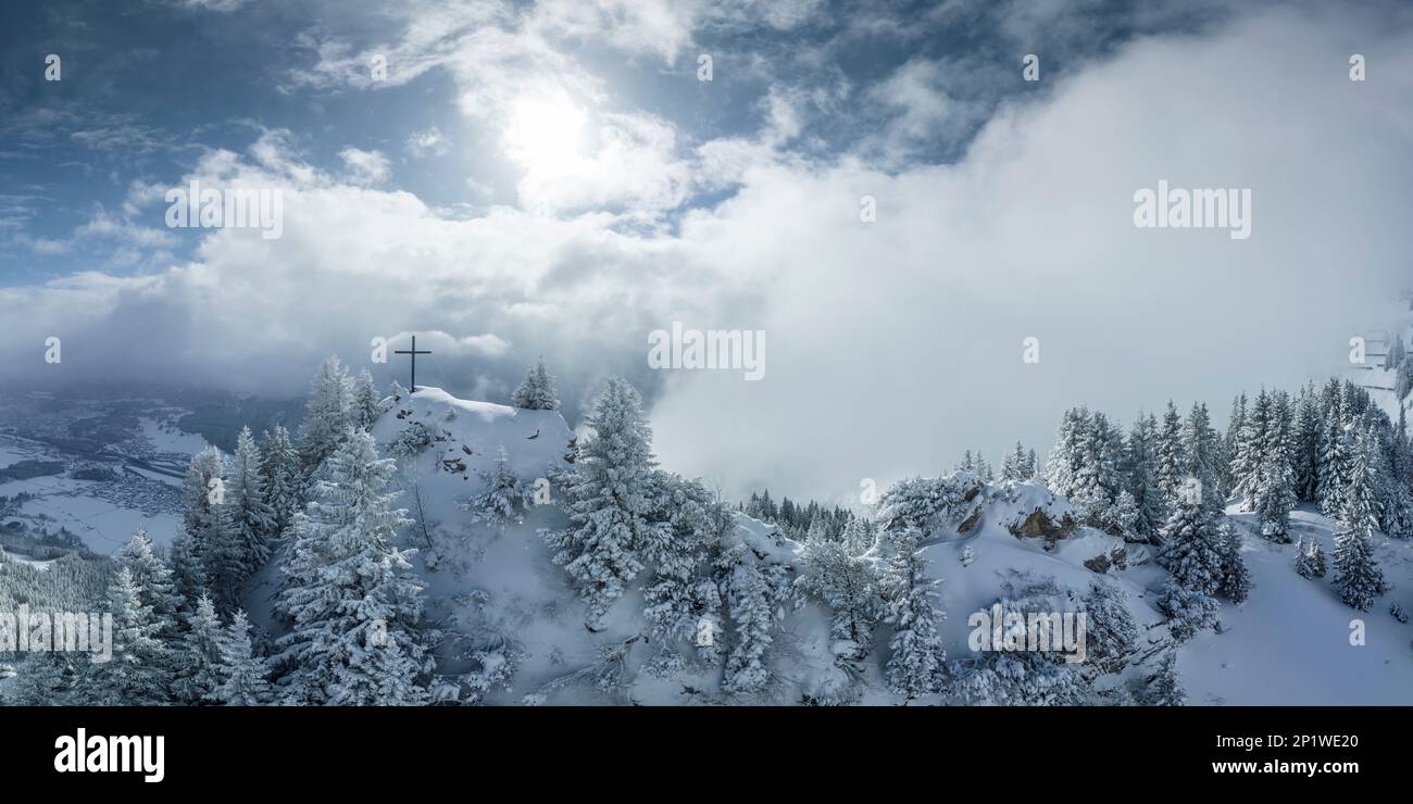 Espectacular cruz de cumbre iluminada por el sol de la mañana en el pico de la montaña Hahnenkamm recién cubierto de nieve en Austria Foto de stock