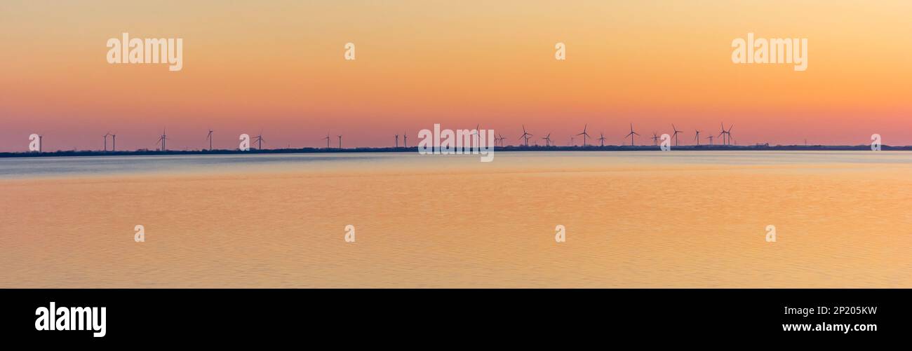 Muchas turbinas de viento en el agua contra un cielo colorido en Wilhelmshaven, Alemania Foto de stock