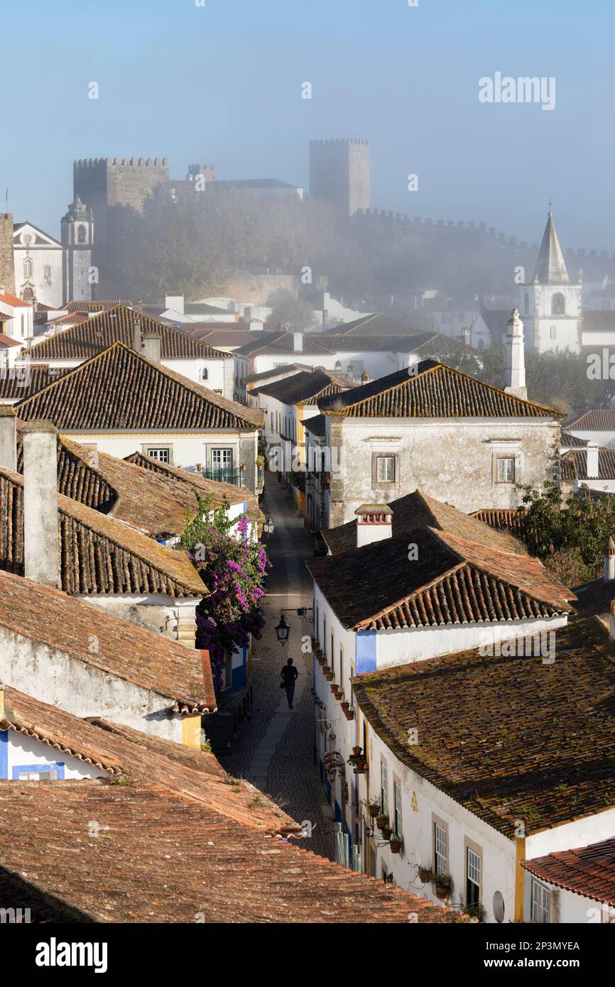 Vista a lo largo de Rua Direita en el casco antiguo y las paredes de Obidos en la niebla de la mañana, Obidos, Región Central, Portugal, Europa Foto de stock