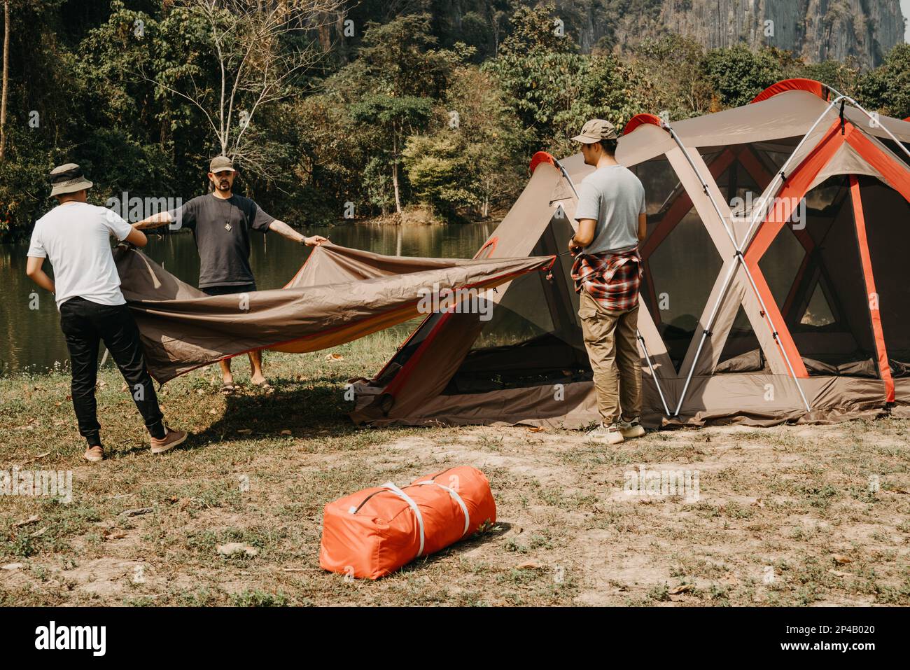 Los hombres jóvenes ayudan a establecer tiendas de campaña para acampar. Foto de stock