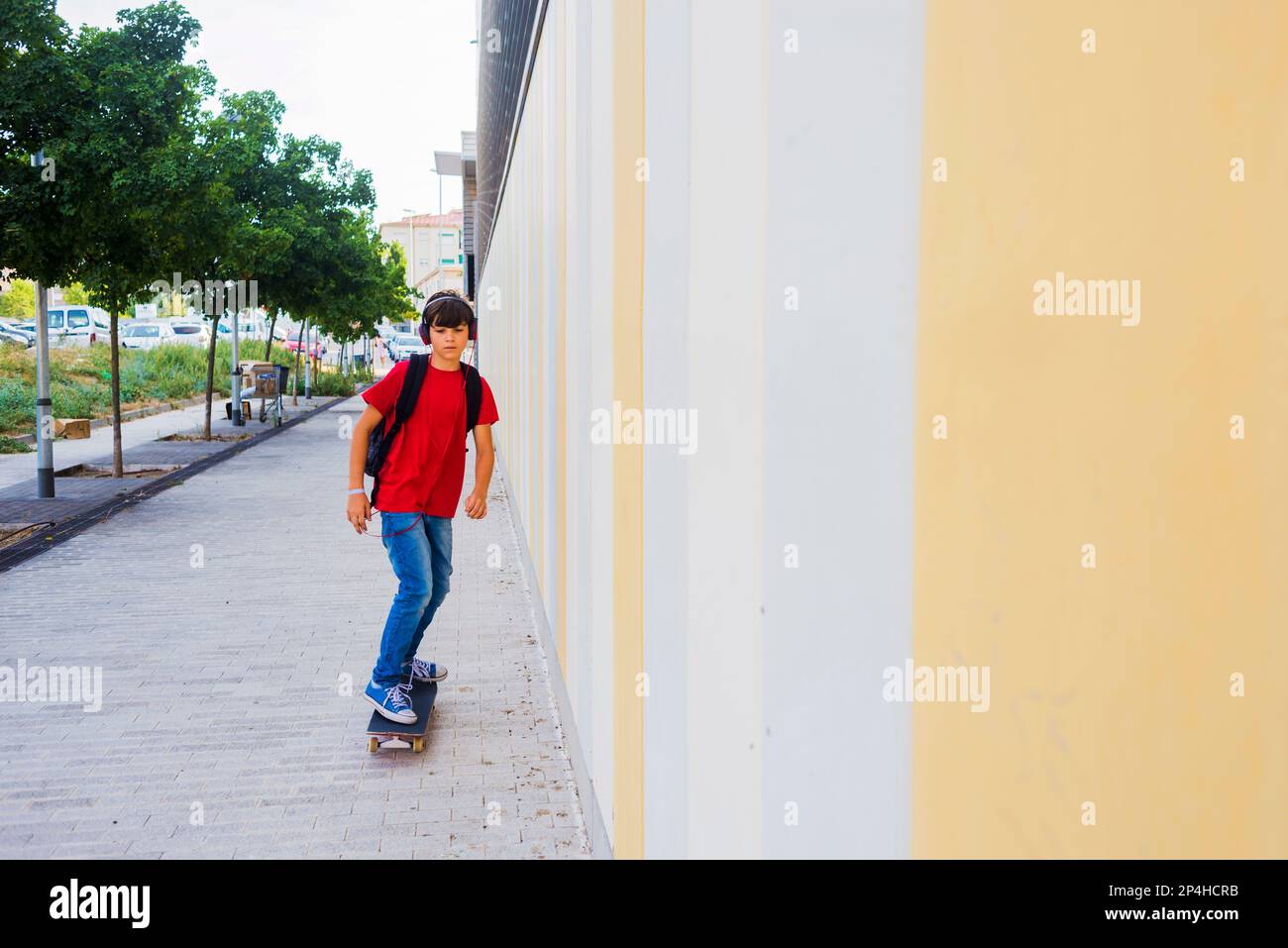 Vista frontal de un niño joven patinando contra una pared de color Foto de stock