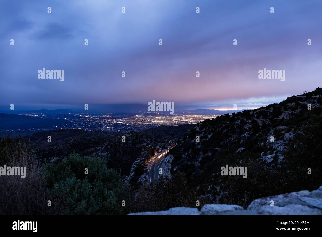 Una vista nocturna de Tucson, Arizona, visto desde arriba en las montañas de Santa Catalina. Los faros de un vehículo se ven moviéndose por una montaña. Foto de stock