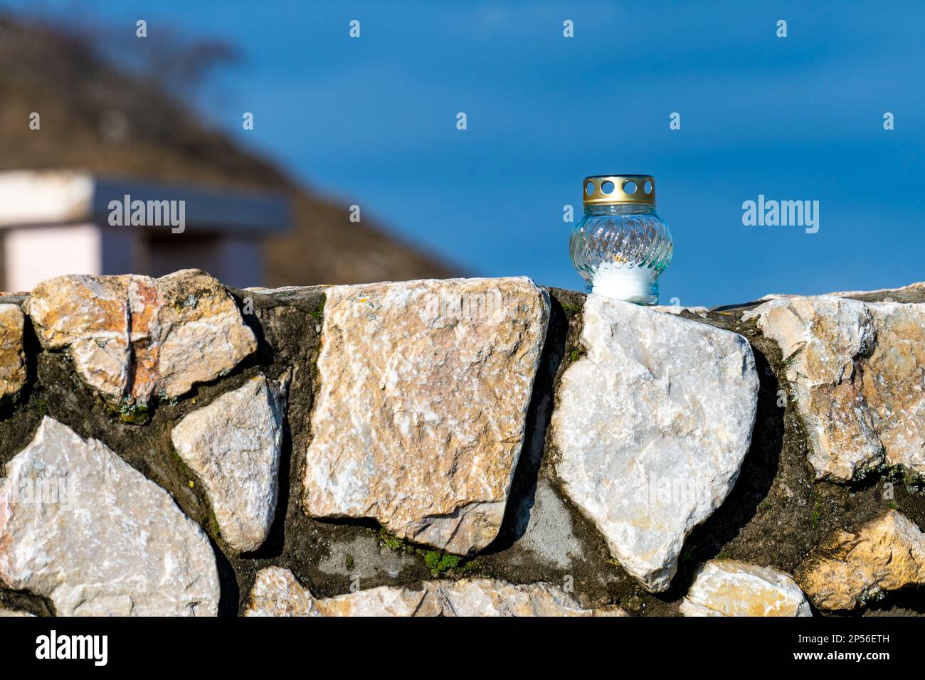 Vela de vidrio transparente ardiendo en una pared de piedra frente a un cielo azul Foto de stock