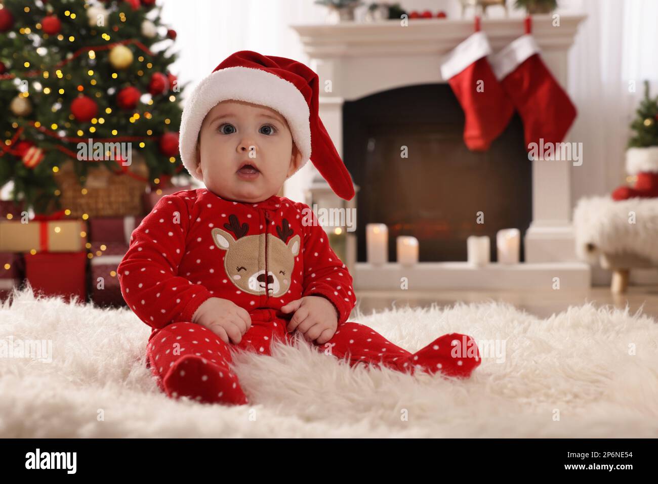 Bebé en sombrero de Santa y pijamas de Navidad brillante en el piso en casa  Fotografía de stock - Alamy