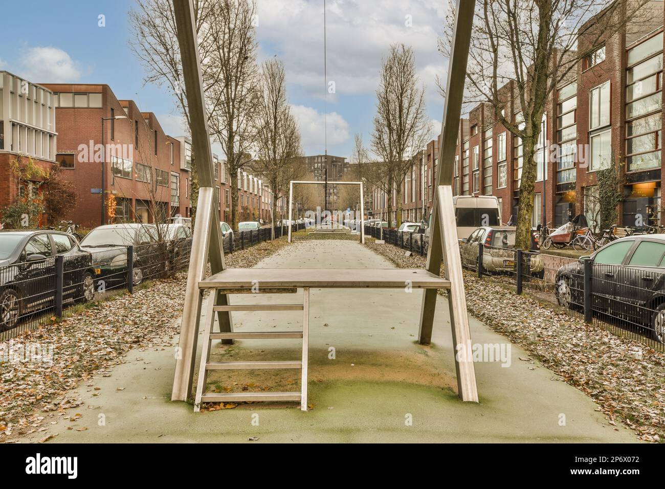 un banco vacío en medio de una calle con coches estacionados a ambos lados  y árboles que crecen a lo largo de la acera Fotografía de stock - Alamy