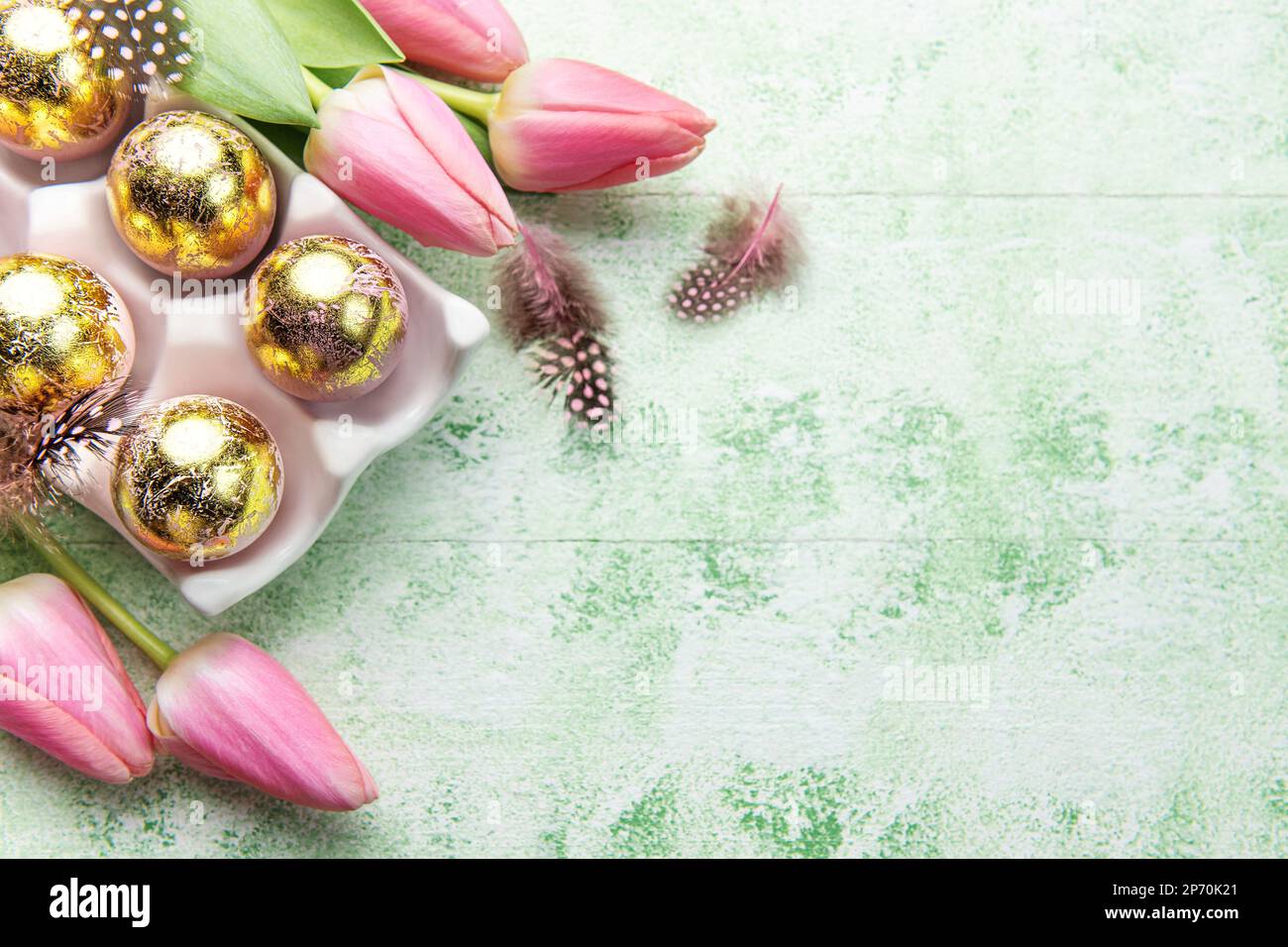Soporte con huevos de Pascua pintados de colores dorados y tulipanes rosados sobre un fondo de madera verde. Vista superior. Espacio para texto. Foto de stock