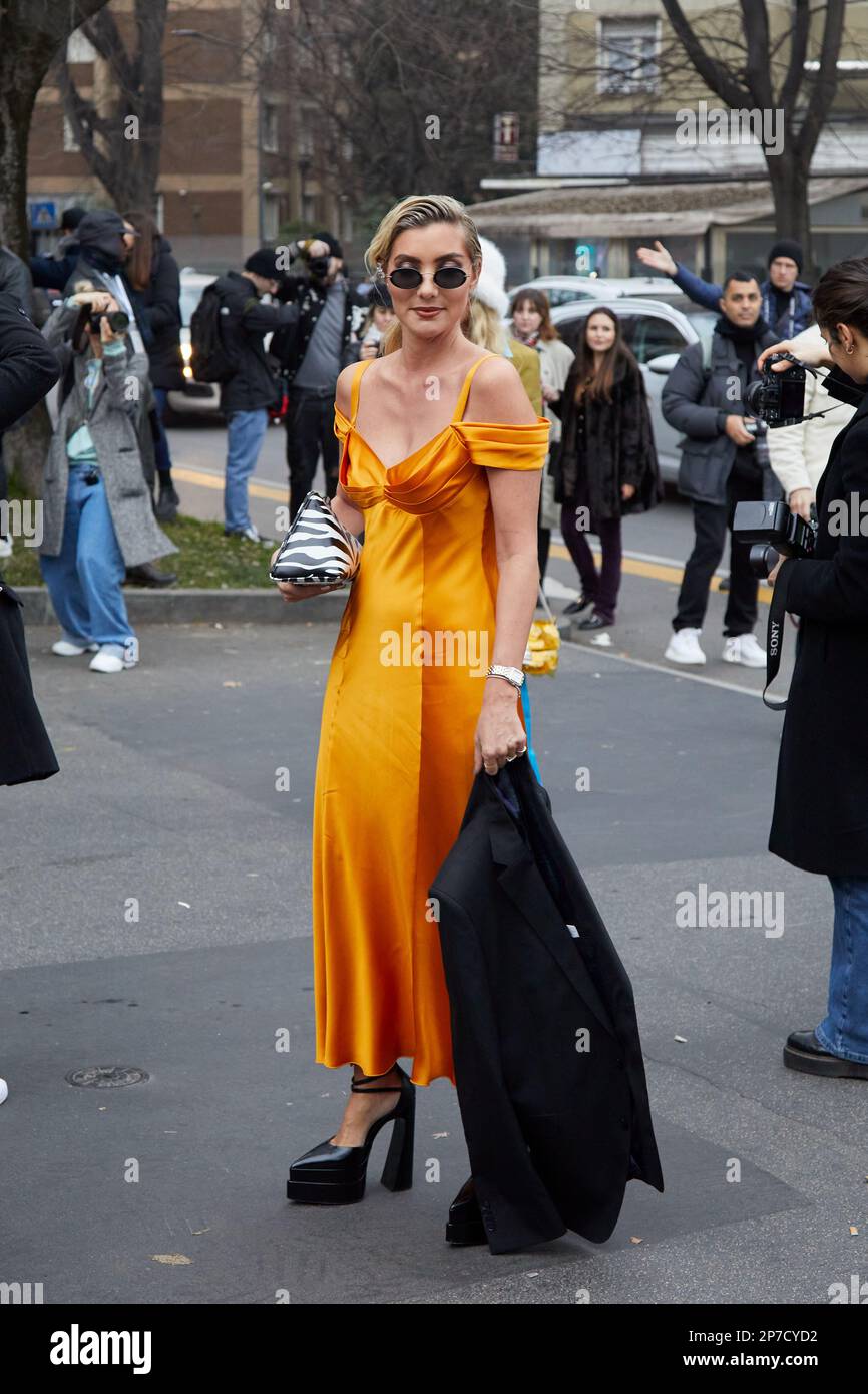 MILÁN, ITALIA - 22 DE FEBRERO de 2023: Mujer con vestido naranja y chaqueta negra antes del desfile de Alberta Ferretti, estilo callejero de la Semana de la Moda de Milán Foto de stock