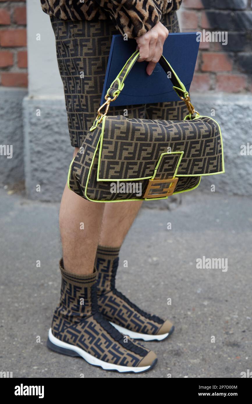 MILÁN, ITALIA - 22 DE FEBRERO de 2023: Hombre con pantalones cortos con logotipo Fendi marrón y negro, bolso y patrón de zapatillas antes del desfile de Fendi, Milan Fashion Week s Foto de stock