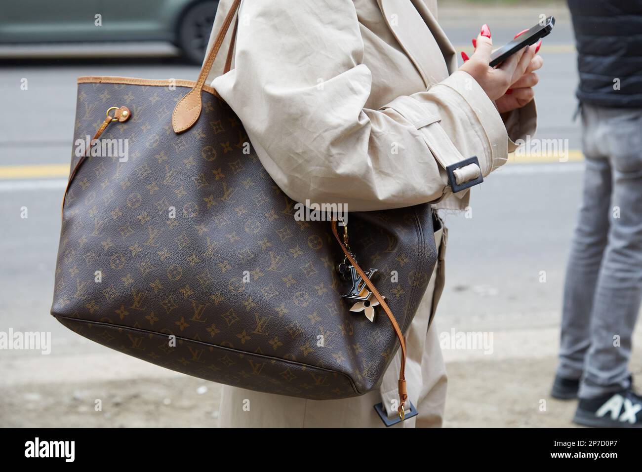 MILÁN, ITALIA - 22 DE FEBRERO de 2023: Mujer con bolso Louis Vuitton marrón y gabardina beige antes del desfile de Fendi, estilo callejero de la Semana de la Moda de Milán Foto de stock