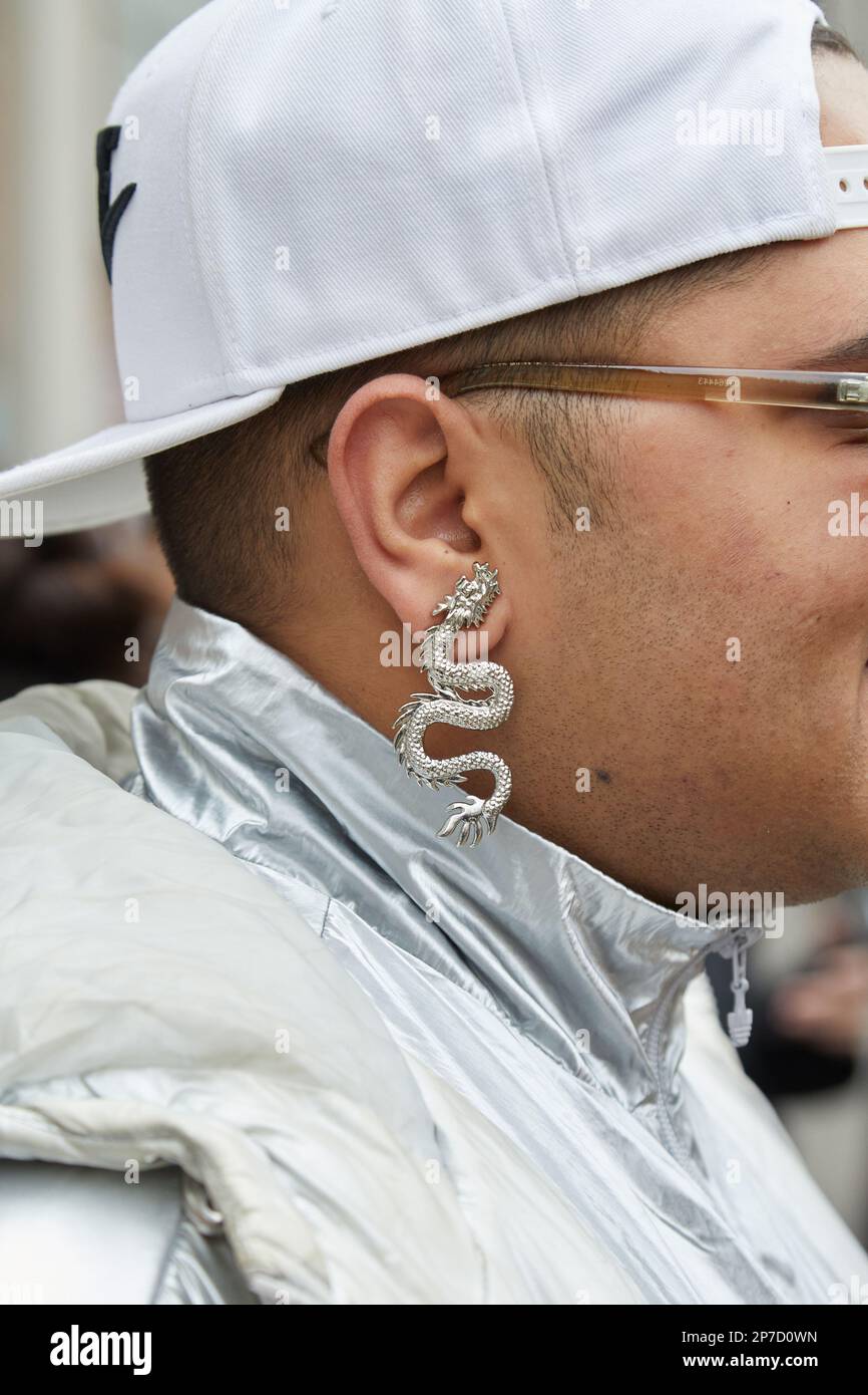 MILÁN, ITALIA - 22 DE FEBRERO de 2023: Hombre con pendiente de dragón de plata, gorra blanca y chaqueta de plata antes del desfile de Fendi, Milan Fashion Week street sty Foto de stock