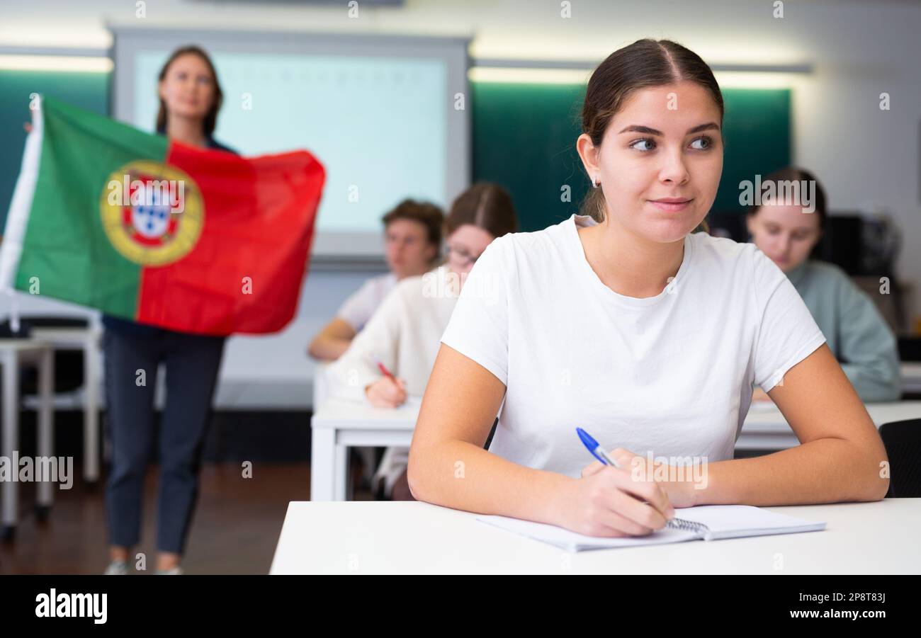 El profesor habla sobre el país y la bandera nacional de Portugal en una lección de geografía. Los estudiantes adolescentes escuchan con atención Foto de stock