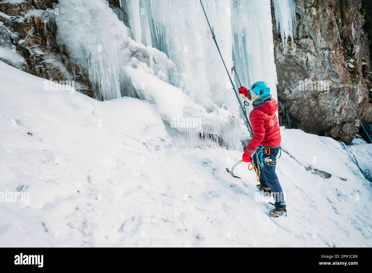 Escalador de hielo vestido ropa cálida de escalada de invierno, arnés de seguridad y casco bajo la cascada congelada. Personas activas y actividades deportivas concepto im Foto de stock