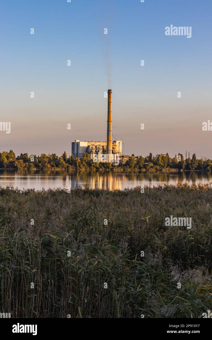 Contra un cielo colorido, las chimeneas de plantas de procesamiento de residuos en un lago emiten humo. Aunque la energía se genera, conduce a la contaminación ambiental. Foto de stock