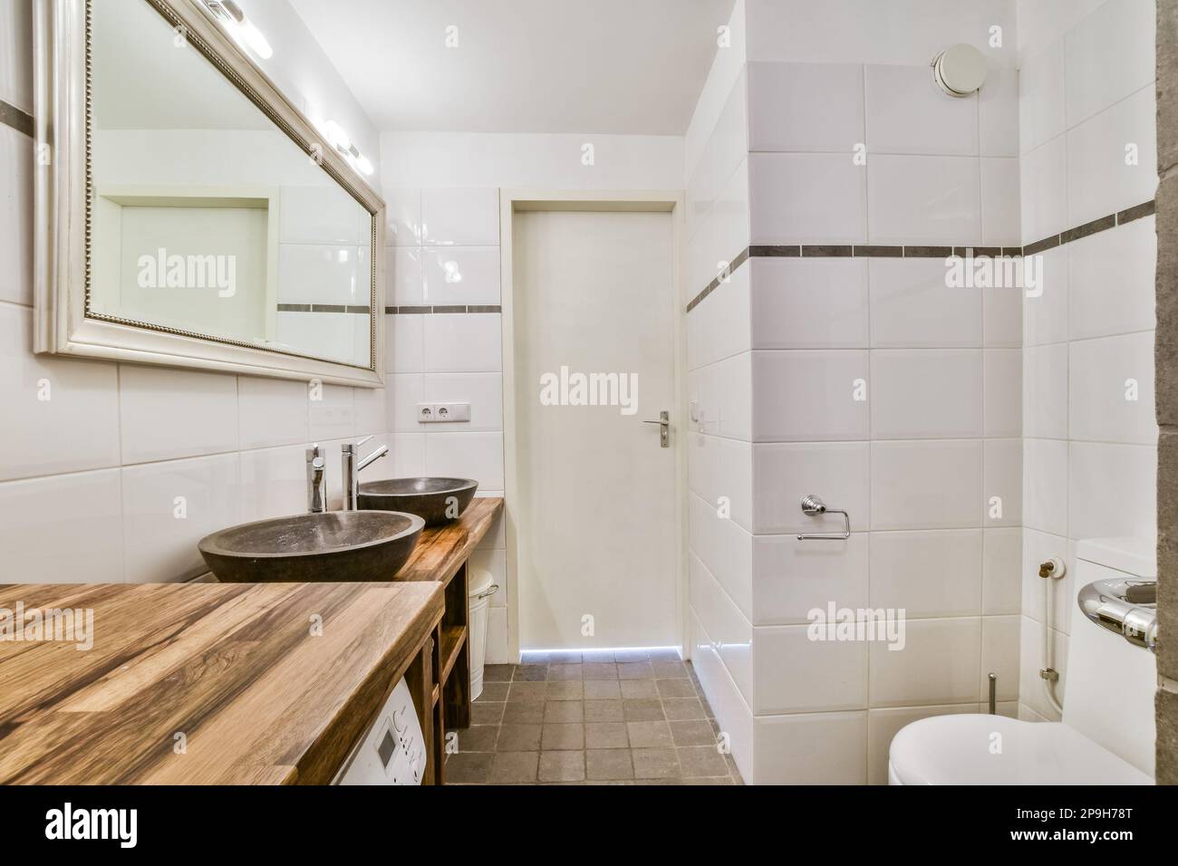 un cuarto de baño con lavabo, inodoro y mostrador de madera en las esquinas en el lado izquierdo de la habitación Foto de stock