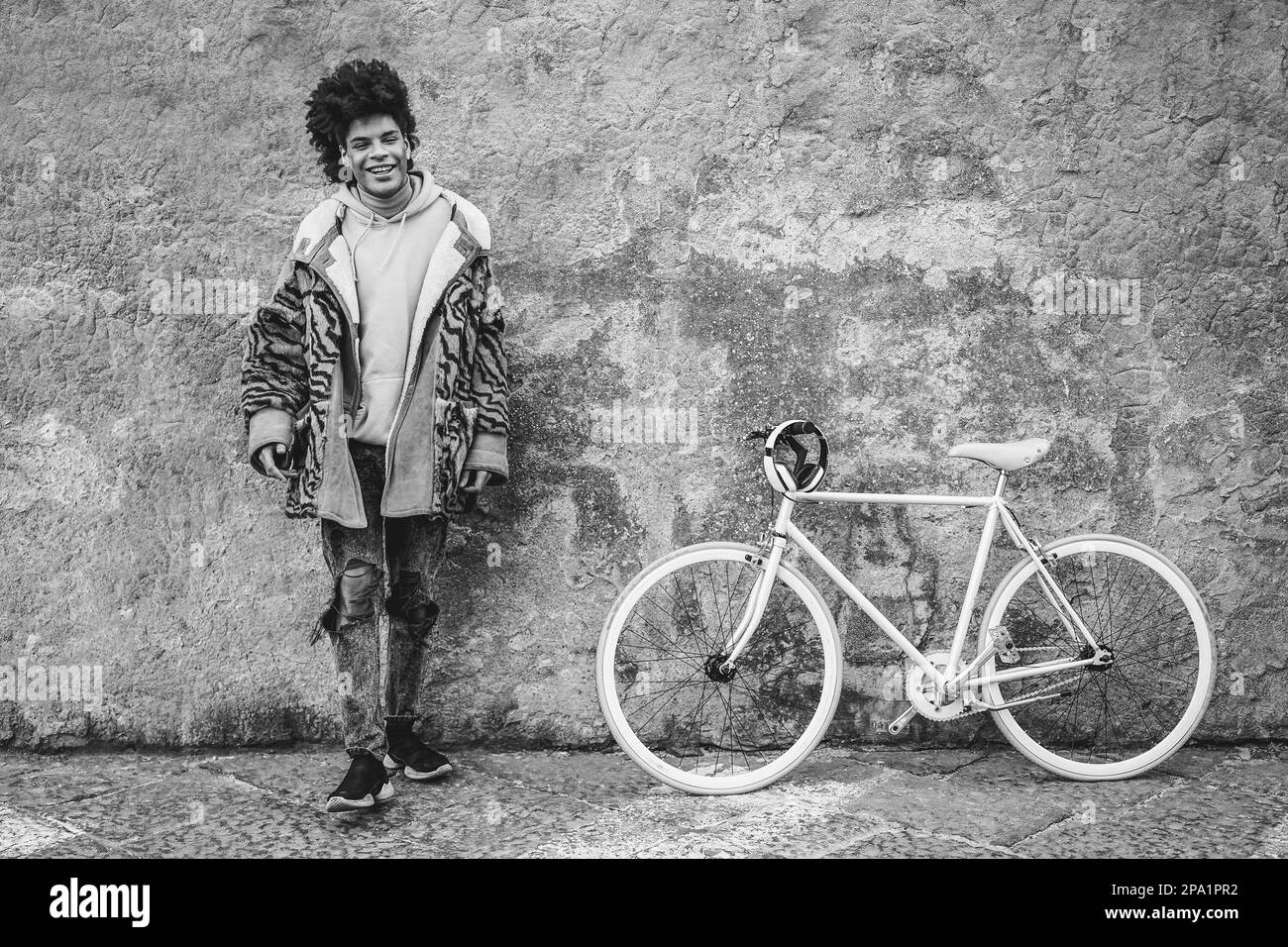 Niño africano joven que se divierte con su bicicleta al aire libre en la ciudad - Enfoque suave en la cara - Edición en blanco y negro Foto de stock