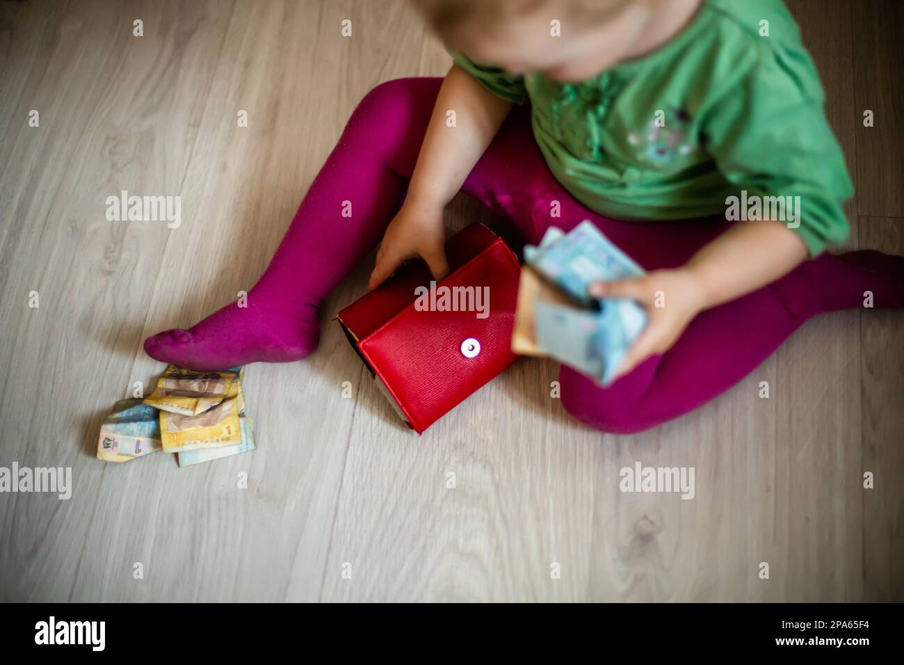 Niña niño con monedero rojo y billetes en las manos se sienta en la habitación en el piso. el niño juega con el dinero. Crisis financiera. Bolso vacío. Foto de stock