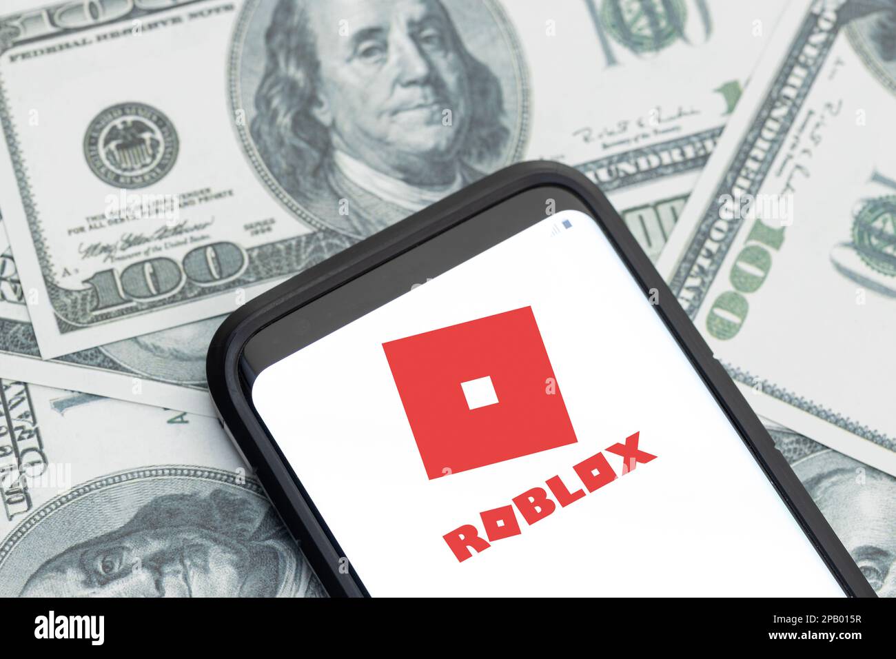 Galicia, España; 12 de marzo de 2023: Logotipo de la empresa Roblox en la pantalla del smartphone y fondo de billetes en dólares Foto de stock