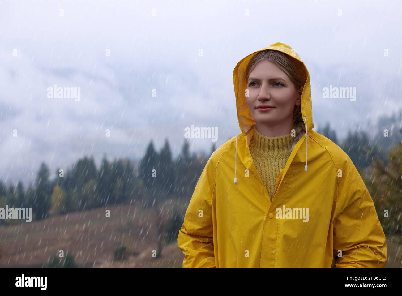 Mujer joven en chubasquero disfrutando del paisaje de montaña bajo la lluvia Foto de stock