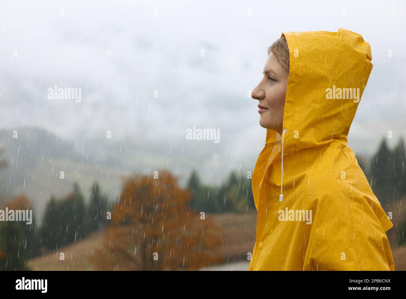 Mujer joven en chubasquero disfrutando del paisaje de montaña bajo la lluvia Foto de stock