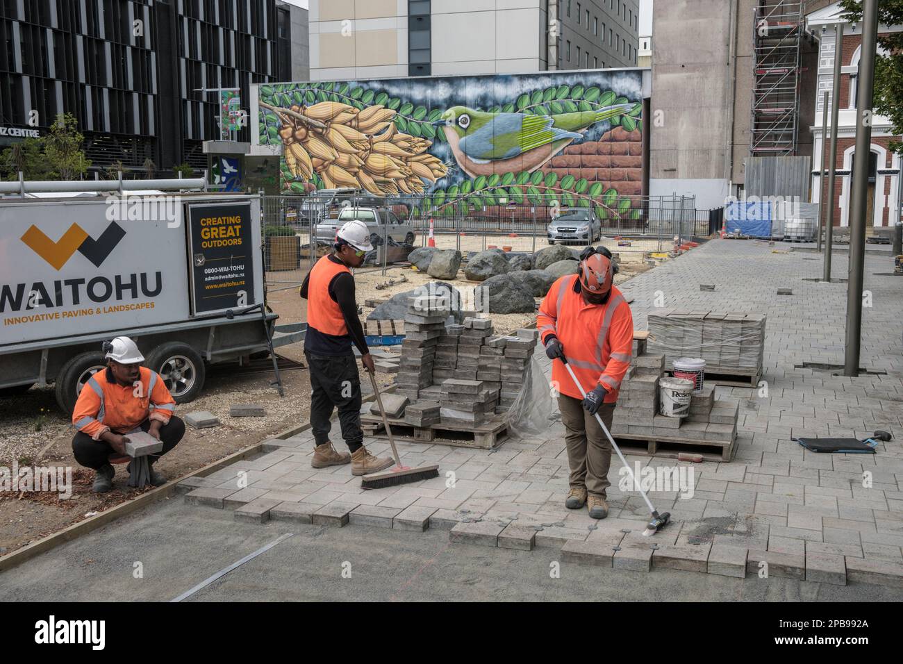 Trabajadores que ponen ladrillos de pavimentación con un telón de fondo de arte callejero en Christchurch, Isla Sur, Nueva Zelanda Foto de stock