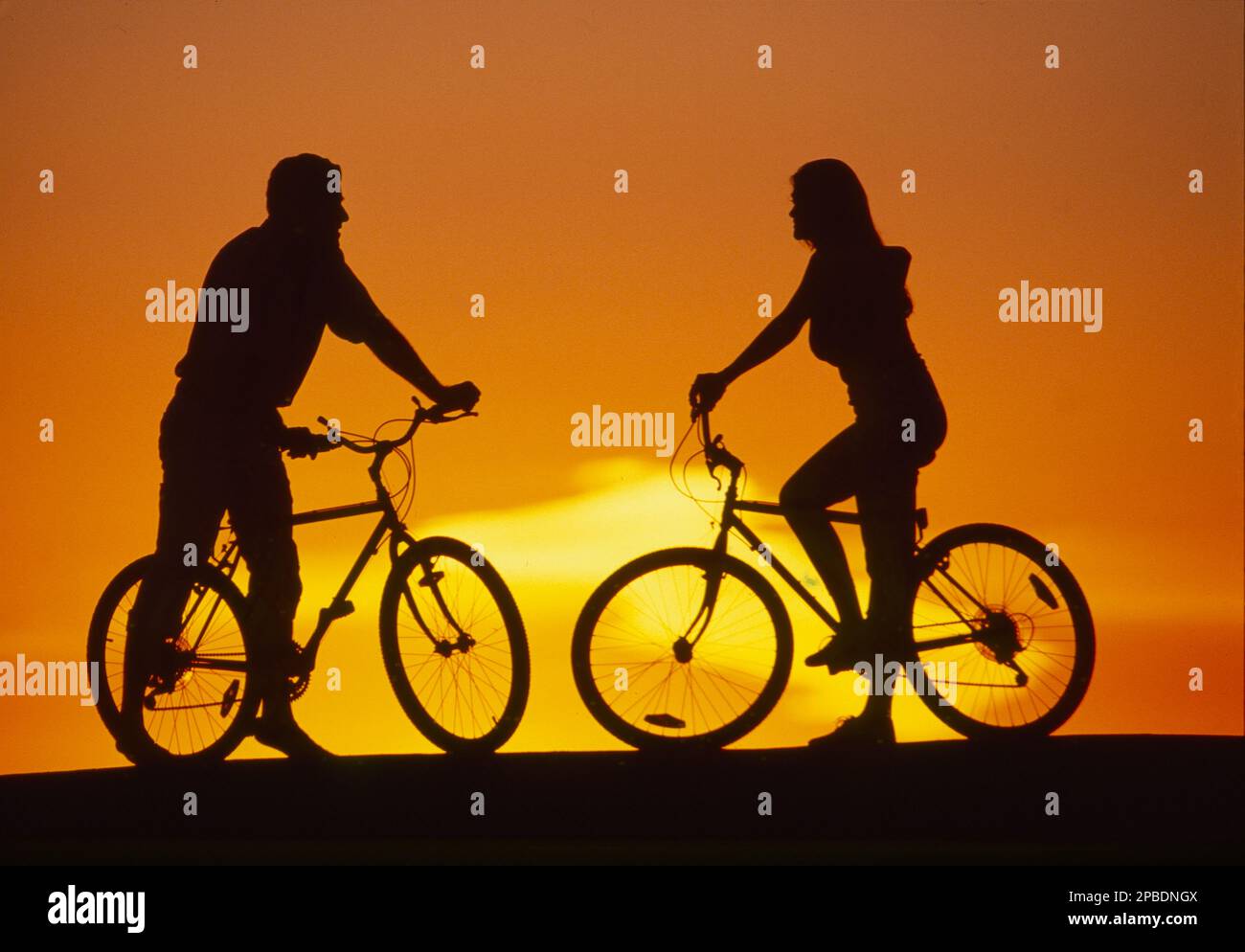 Pareja en bicicletas frente a la otra silueta contra la puesta de