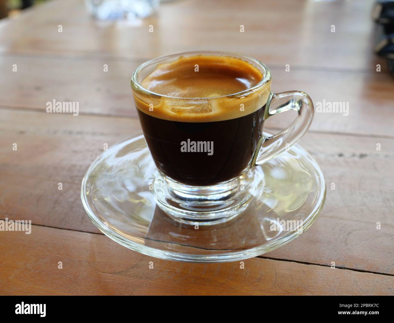 Café espresso caliente en una taza de vidrio transparente con crema en la mesa de madera Foto de stock