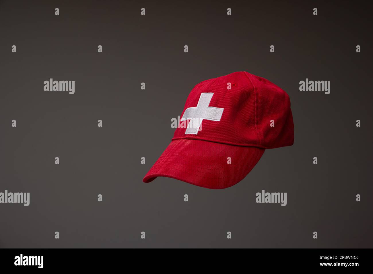 Gorra de béisbol roja con bandera suiza cruz blanca. Close up studio shot, aislado sobre fondo gris. Foto de stock