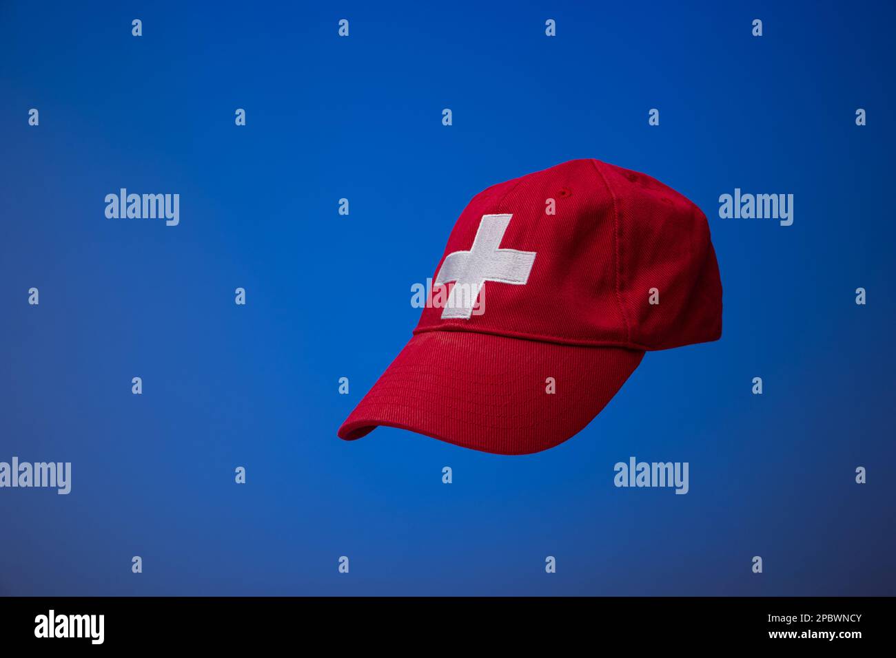 Gorra de béisbol roja con bandera suiza cruz blanca. Cerca de tiro de estudio, aislado sobre fondo azul. Foto de stock