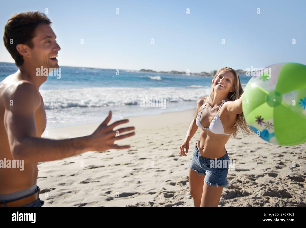 Ella siempre gana (porque la dejo). Una joven pareja jugando con una pelota de playa. Foto de stock