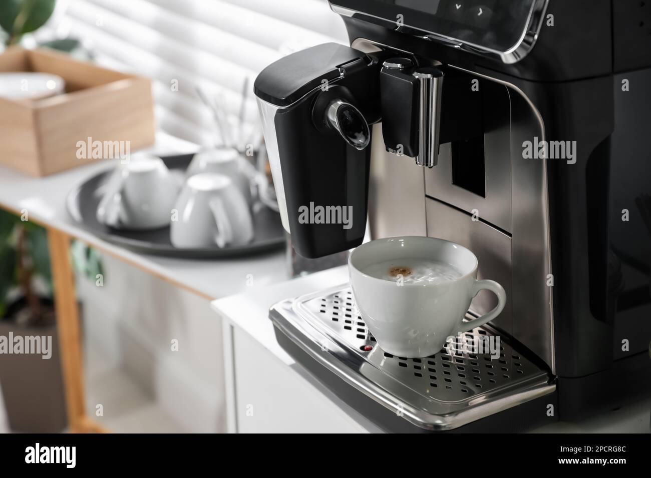 Moderna máquina de café con taza de capuchino en la oficina