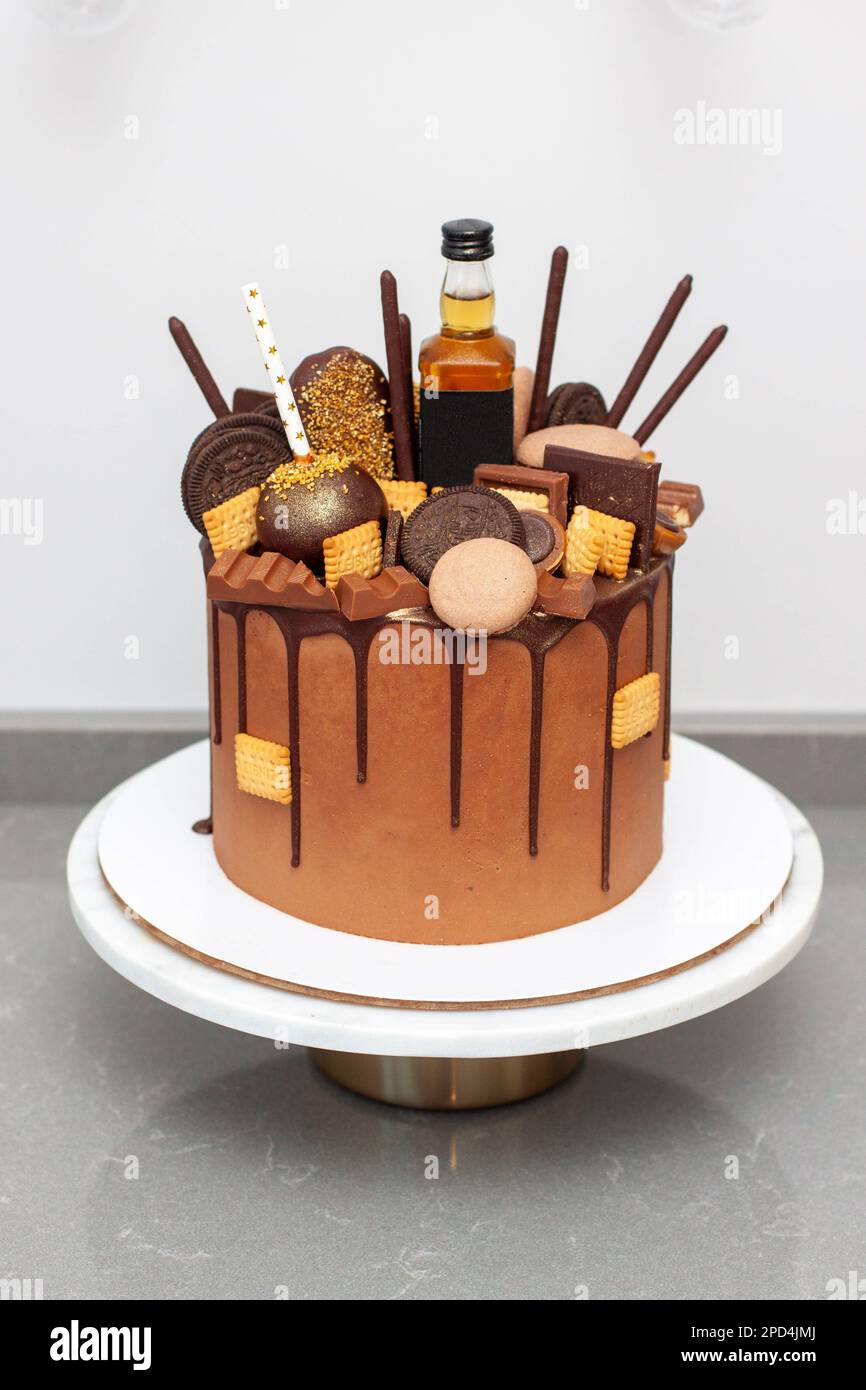 Precioso pastel de chocolate de cumpleaños lujosamente decorado con  bombones y dulces, con botella de alcohol fuerte en la parte superior.  Regalo para un hombre joven Fotografía de stock - Alamy