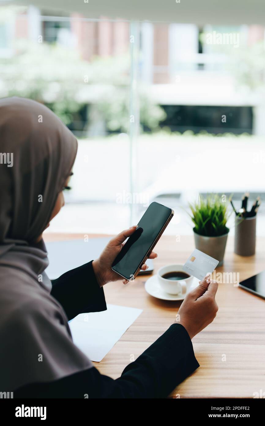 Foto Hermosa mujer musulmana con ropa formal y hiyab haciendo compras en  línea con tarjeta de crédito y teléfono inteligente. Joven de pie cerca del  edificio de oficinas y disfrutando de un