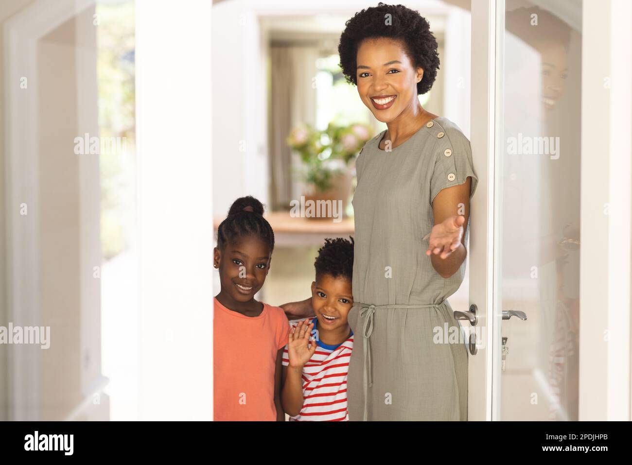 Retrato de madre afroamericana feliz y niños que abren la puerta e invitan Foto de stock