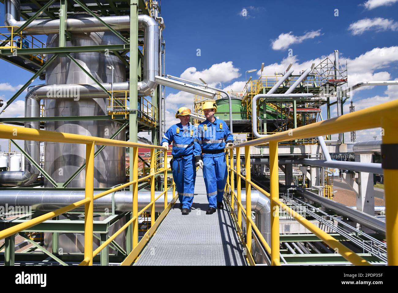 planta de la industria química - trabajadores en ropa de trabajo en una refinería con tuberías y maquinaria Foto de stock