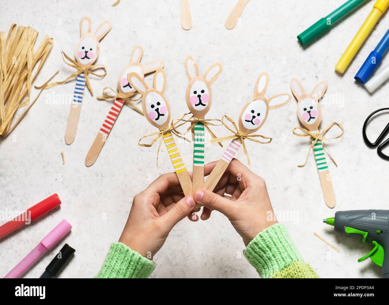Vista superior de tres conejitos divertidos coloridos hechos a mano de cucharas de madera en manos de niños. Pequeño regalo o decoración para Pascua. Fácil diversión niños manualidades concepto Foto de stock