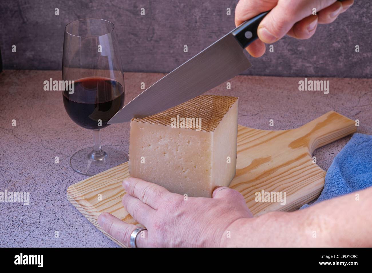 Cortar queso manchego con un cuchillo en una tabla de madera y una copa de  vino tinto para acompañar el almuerzo Fotografía de stock - Alamy