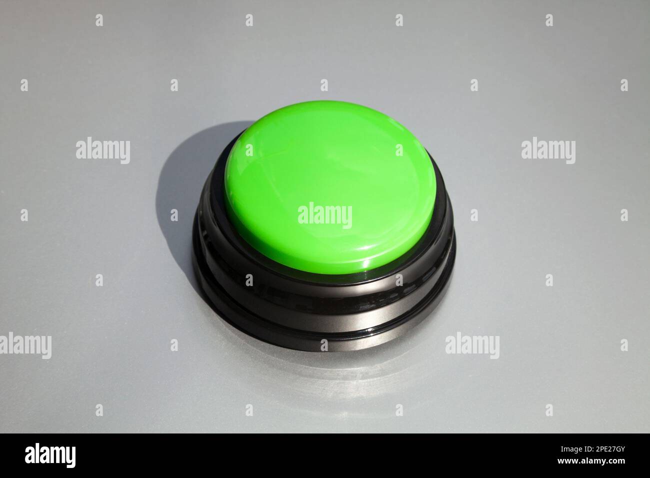 Zumbador verde grande para respuestas en un programa de juego aislado en gris. Botón inalámbrico para enseñar a los niños o entrenar animales Foto de stock
